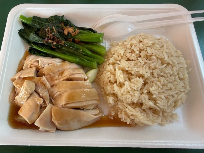 A takeout container filled with a meal of sliced poached chicken, and rice.