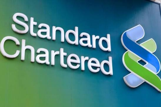 A close-up of a Standard Chartered bank sign featuring its white text and blue and green logo on a teal background.