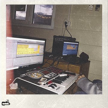 The image shows a person sitting at a desk with two keyboards, one of which has a music track playing on it. The person appears to be working or creating music using these instruments. The background features a window that allows natural light into the room, suggesting an indoor setting like a home office or studio.