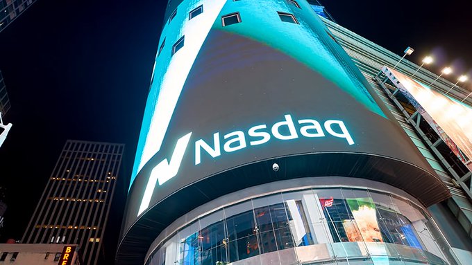 An illuminated Nasdaq sign displayed on the curved facade of a building at night, shot from a low angle.