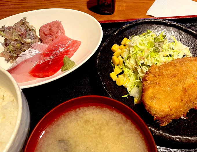 Japanese meal featuring a sashimi bowl with tuna and beef, a breaded cutlet with cabbage and corn salad, miso soup, and rice.