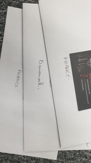 Three white envelopes labeled "FRANCE," "Denmark," and "KONACE" lying on a granite countertop, accompanied by a black business card for what appears to be a security company.
