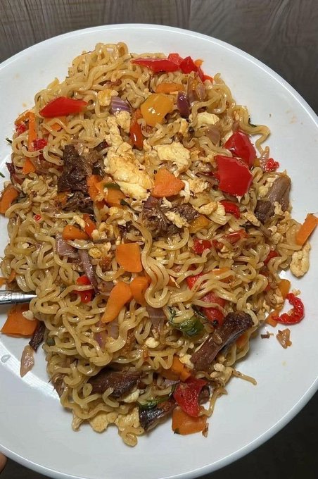 A close-up photo of a plate of stir-fried ramen noodles mixed with beef, red bell peppers, carrots, onions, and scrambled eggs.
