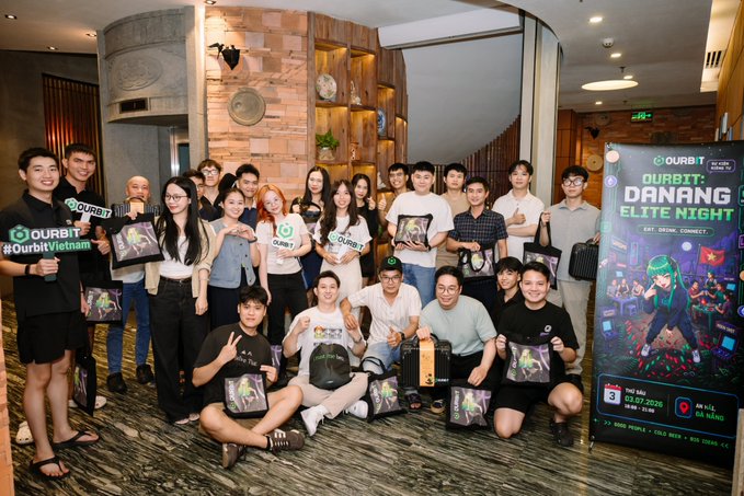 Group photo of attendees at the 'OURBIT: DAN4ING ELITE NIGHT' event in HCMC on 03.07.2026, with participants holding branded OURBIT merchandise and standing next to an event banner.