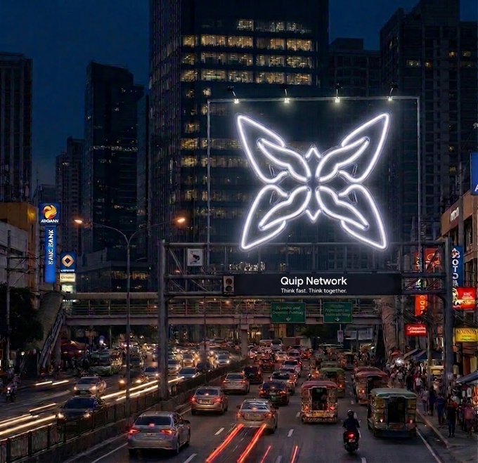 Nighttime cityscape with traffic on a busy road beneath an elevated highway displaying a large illuminated Quip Network logo with the tagline 'Think fast. Think together.'