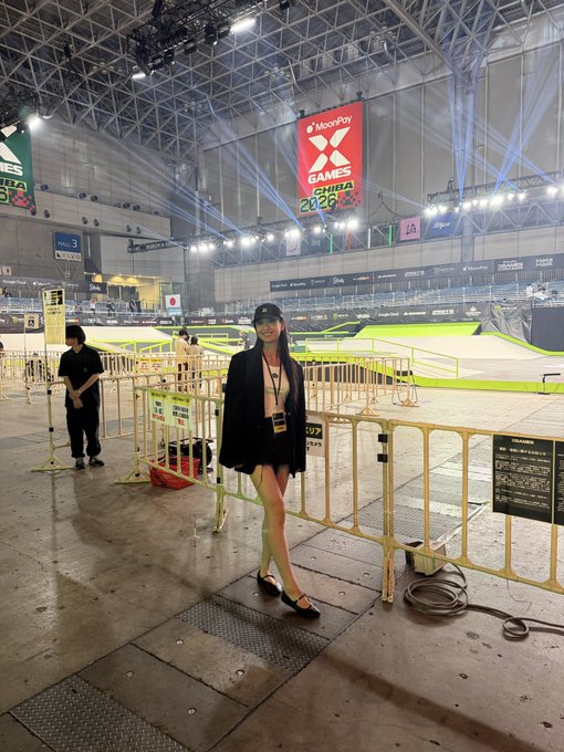 A woman wearing a black cap and lanyard poses at the X Games Chiba 2026 venue, with a prominent red "MoonPay X GAMES CHIBA 2026" banner hanging from the ceiling above the skateboarding arena, highlighting the MoonPay partnership with the event.