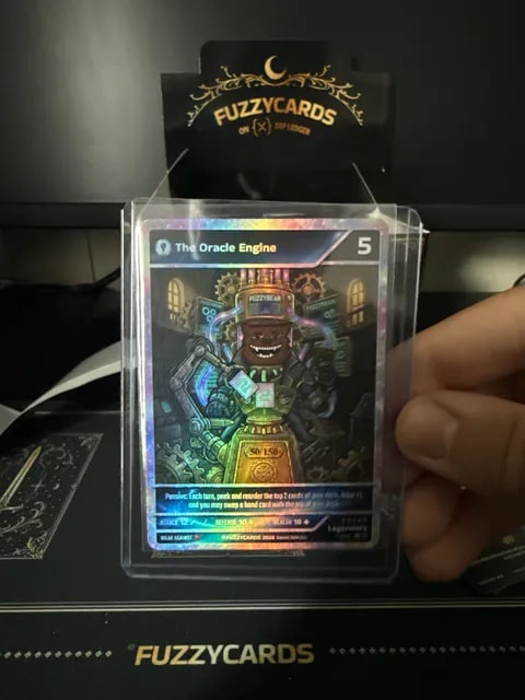 A hand holds a holographic trading card titled "The Oracle Engine" (cost 5) in a protective sleeve, displayed in front of a "FUZZYCARDS" branded box.