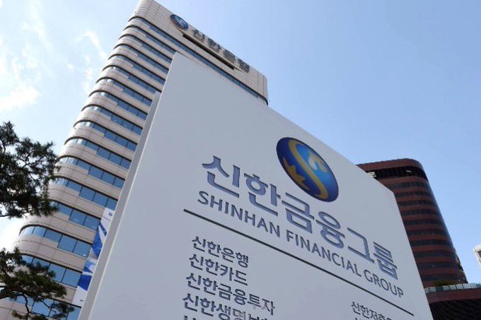 A low-angle shot of the 'SHINHAN FINANCIAL GROUP' building, featuring its logo and Korean text ('신한금융그룹') on a sign in the foreground.