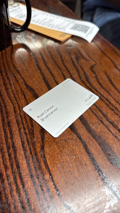 A Visa debit card with the name "Ryan Carson" sits on a wooden table, tied to a receipt from a restaurant. The image illustrates the creator's point about X creator payments being loaded onto his X Money card, which he used to pay for the breakfast outing.
