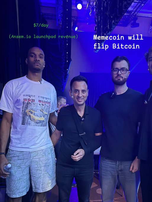 A photo from what appears to be a crypto event, with overlaid text reading "$7/day (Ansem.io launchpad revenue)" in green and "Memecoin will flip Bitcoin" in white, showing several men standing on a stage under purple lighting—including one wearing a racing-themed t-shirt—capturing the bullish, meme-driven crypto culture referenced in the post's claim about memecoins overtaking Bitcoin.