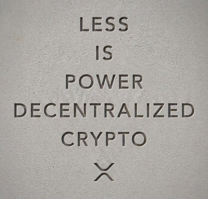 Text engraved or printed on a stone-like surface reading "LESS IS POWER DECENTRALIZED CRYPTO" with an X-shaped logo below.