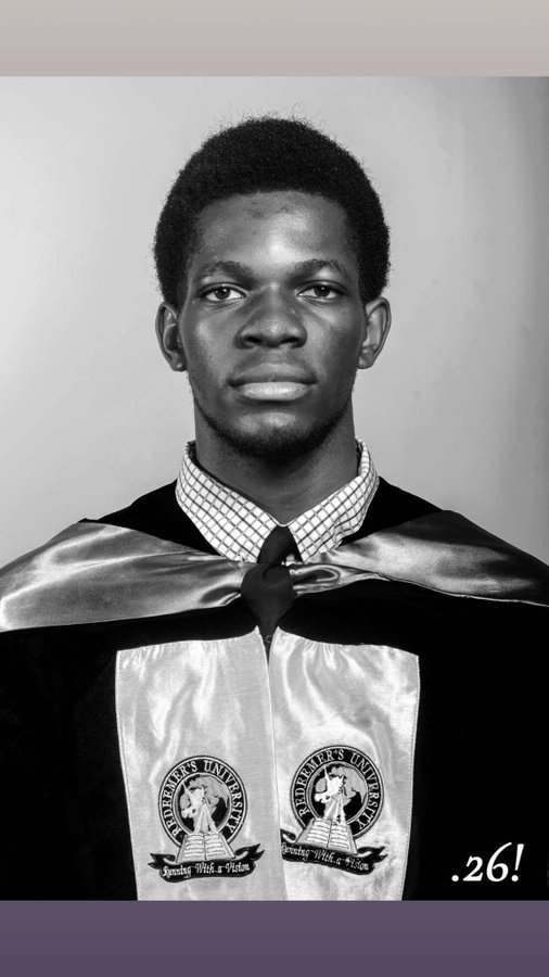A young man poses in a black graduation gown with a checkered shirt and tie, wearing a Southeastern University stole adorned with two crests reading "Spreading Wit & Wisdom." The ".26!" watermark reinforces the post's theme of celebrating the number 26, tying his graduation milestone to his personal lucky number and aspirations.