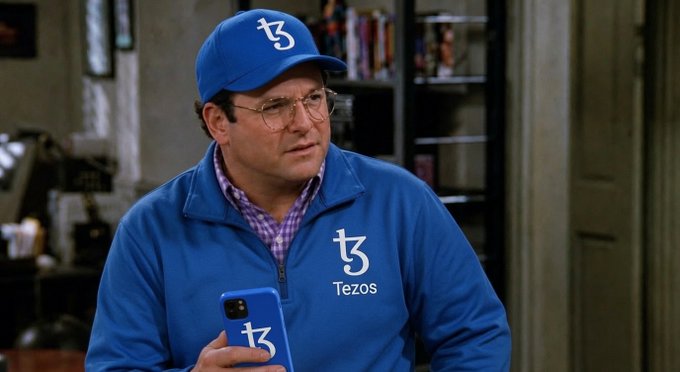 A man wearing a blue Tezos-branded cap, jacket, and phone case (featuring the tz logo) stands in what appears to be an apartment setting, styled like a meme referencing the 'Tezos' cryptocurrency.