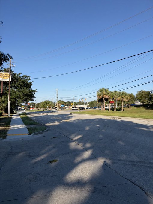 A view of a street intersection under a clear blue sky, with palm trees, power lines, and a 'Night In White Satin' sign visible.