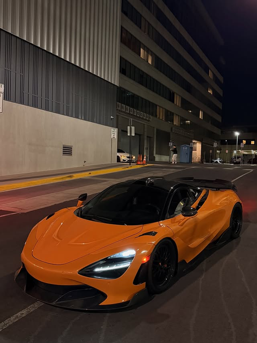 An orange McLaren supercar sits parked at night under streetlights, its sleek design and illuminated headlights standing out against the urban backdrop, complementing the post's crypto giveaway vibe with luxury and exclusivity.
