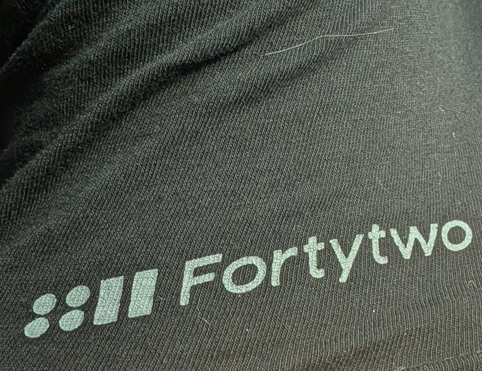 Close-up of dark fabric with silver text reading "FORTYTWO" alongside a logo of four shapes (two circles and two vertical bars).