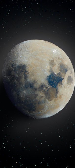 A detailed astronomical image of a moon or planet with a cratered, mottled surface of beige and dark gray regions, set against a starry black space background.