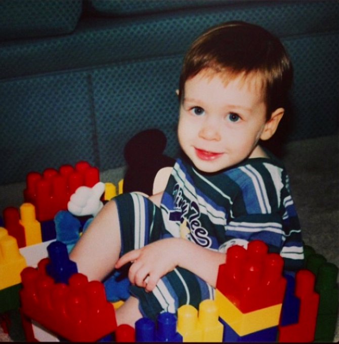 Vintage photograph of a smiling young child in a blue and white striped shirt sitting in a colorful plastic block playset.