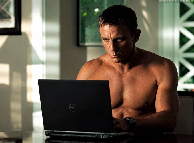 A shirtless man intently types on a Dell laptop in a sunlit room, humorously channeling the spirit of someone turning to AI for crypto market analysis. The image plays on the relatable "consulting every possible source" approach to forecasting Bitcoin's price movements.