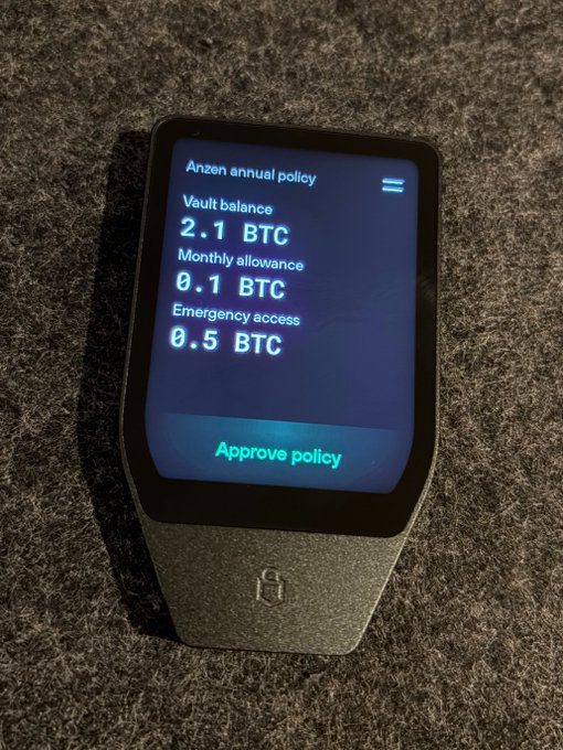 A Trezor hardware wallet displays an "Anzen annual policy" with a 2.1 BTC vault balance, 0.1 BTC monthly allowance, and 0.5 BTC emergency access option, ready for approval. The image humorously ties to the post's joke about pre-signed transactions, showcasing how such crypto wallets store and authorize multiple Bitcoin transactions within a single device.