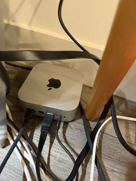 A Mac Mini is shown connected with several cables on a desk, likely behind a piece of furniture. It relates to the post about limited device connectivity, suggesting the Mac Mini is the "local computer" mentioned that can only be accessed by the user's phone.