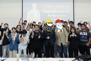 A group photo of people posing together with thumbs up at an event, with some wearing crypto/Bitcoin-themed hats, in front of a screen displaying 'Global Blockchain for Business' with an 'N'x Abstract' logo.