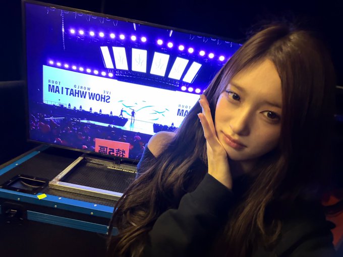A young woman taking a selfie at a gaming/esports event with a large screen behind her showing 'SHOW WHAT I'M MADE' tournament branding.
