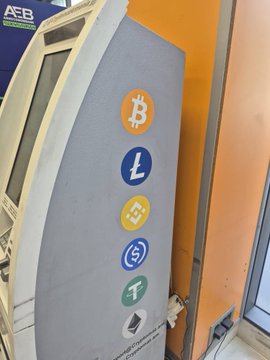 An ATM displaying circular cryptocurrency logos including Bitcoin (B), Litecoin (L), Binance, USDC, Tether, and Ethereum.