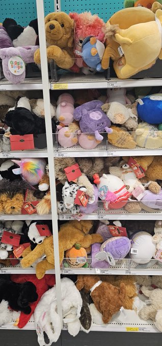 Store shelves densely stocked with various colorful stuffed animals including teddy bears, octopuses, and other plush toys, many with price tags and red sale stickers.