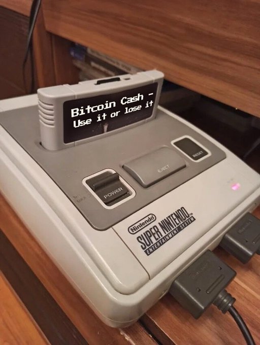 A Super Nintendo Entertainment System console sits on a wooden surface, with its controller slot displaying the message 'Bitcoin Cash - Use it or lose it'.
