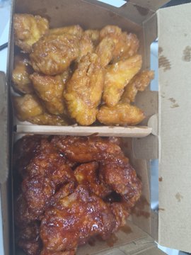 An open cardboard box containing two types of fried chicken wings, with lighter golden wings on top and darker, glazed reddish wings on the bottom.