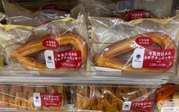 Shelf in a Japanese bakery displaying packaged milk chocolate cookies (125円 and 128円) and soft coffee cream bread (164円).