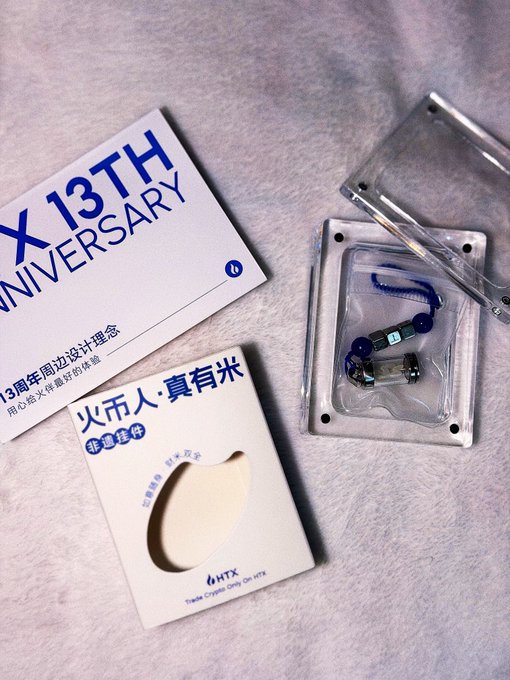 Huobi HTX's "X 13th Anniversary" merchandise box and commemorative crystal display sit alongside a product card reading "火币人·真有米," celebrating the exchange's 13-year milestone of resilience in the crypto industry.