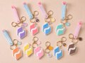 A collection of small pastel-colored acrylic charms or keychains in pink, purple, and yellow shapes arranged on a beige surface.