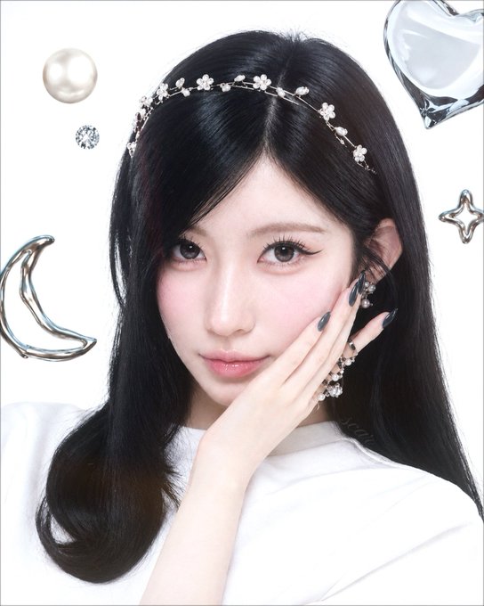 A styled portrait of a young woman with dark hair and a floral headpiece, posing with her hand against her cheek alongside floating decorative elements like pearls, diamonds, a crescent moon, and a heart.