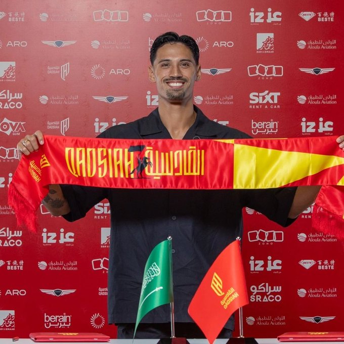A smiling man in a dark shirt holds up a red and yellow 'QADSIAH SC' scarf, standing in front of a red backdrop covered in sponsor logos including 'ARO', 'Aloula Aviation', 'SIXT', and 'QADSIAH', with Saudi Arabian and Al-Qadisiyah flags in front of him.
