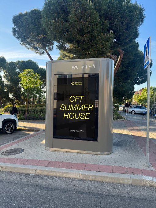 urns of a WCC Summer House sign, with "WCC" and "Summer House" displayed on the top right corner, stand out against a clear blue sky and lush green trees.