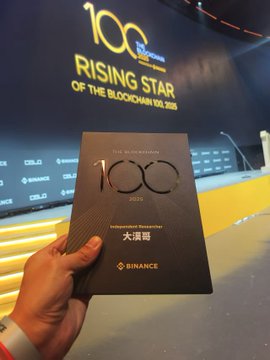 The image features a person holding up an award, possibly for their work or achievements. The award has a black cover with gold lettering that reads "100th", indicating its significance. The background of the image shows a stage setting, suggesting that this event might be related to a performance or competition. The post in the image is about celebrating someone's 100th birthday and includes an award for their work or achievements.