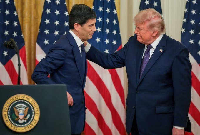 Two men in suits stand together at a podium bearing the Seal of the President of the United States, with American flags behind them.