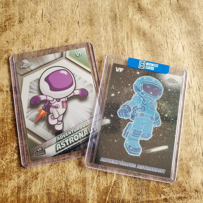 Two Veefriends "Adventurous Astronaut" trading cards sit on a wooden surface, one featuring a purple-suited character from the VF Series 1 "First Chapter" set and the other a blue holographic version with a Midwest Cards sticker, showcasing recent collectibles gifted from fellow Veefriends community members.