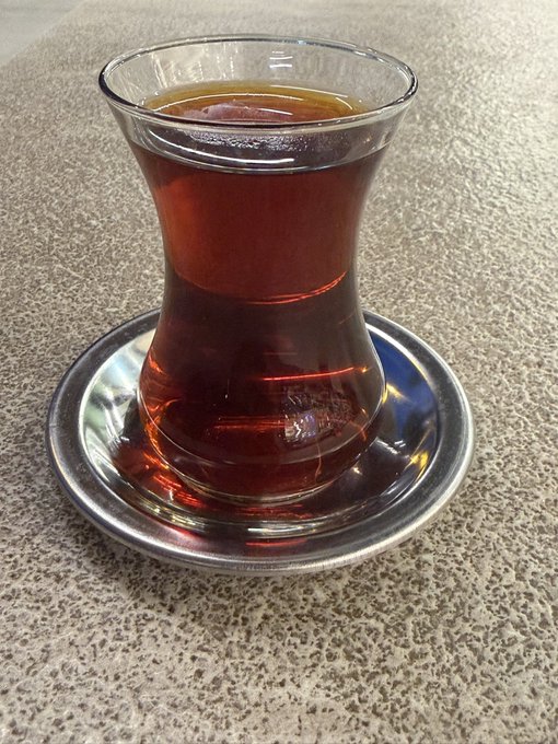 A tulip-shaped glass of dark Turkish tea sits on a silver saucer atop a speckled surface. The image pairs with a morning greeting about a short trade signal triggered after BTC broke 59,500, suggesting the post was shared during a trader's morning tea break.