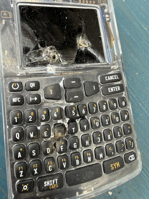 A black hardware wallet with a QWERTY keyboard and visible keys like "CANCEL," "ENTER," "QR," "NFC," and "SHIFT CAPS" lies face-up with its screen severely shattered, reflecting the poster's frustration after destroying their Coinkite device. The cracked display and damaged casing visually echo the post's declaration of lost trust in the Coinkite brand.