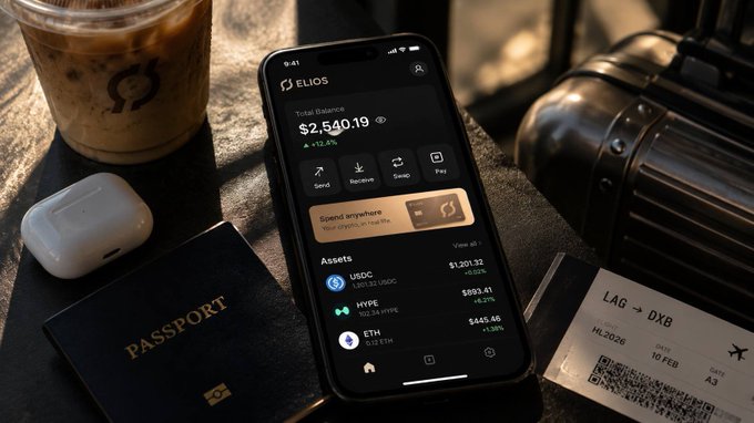 A smartphone displays the Elios app showing a total balance of $2,540.19 alongside crypto assets (USDC, HYPE, ETH), resting on a surface with a coffee, passport, and a Lagos→Dubai (LAG→DXB) boarding pass.