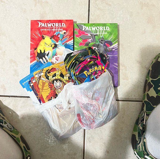 Two 'PALWORLD OFFICIAL CARD GAME' booster packs and several Pokemon cards are displayed next to a plastic bag on a tiled floor, with camouflage shoes visible.