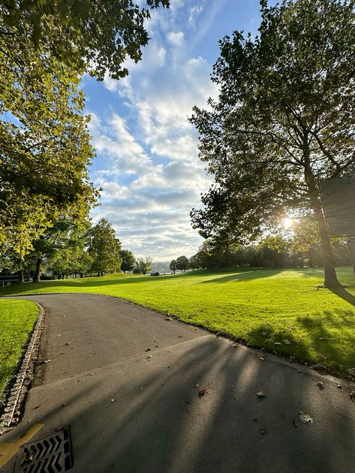 iced-over asphalt road, lined with trees and bushes, leads to a distant hill under a clear blue sky.