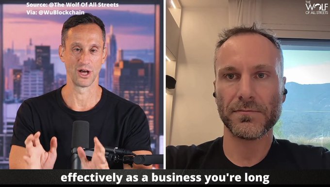 A split-screen video podcast from "Wolf Of All Streets" shows two men conversing, with a subtitle reading "effectively as a business you're long" and credits to @TheWolfOfAllStreets and @WuBlockchain.