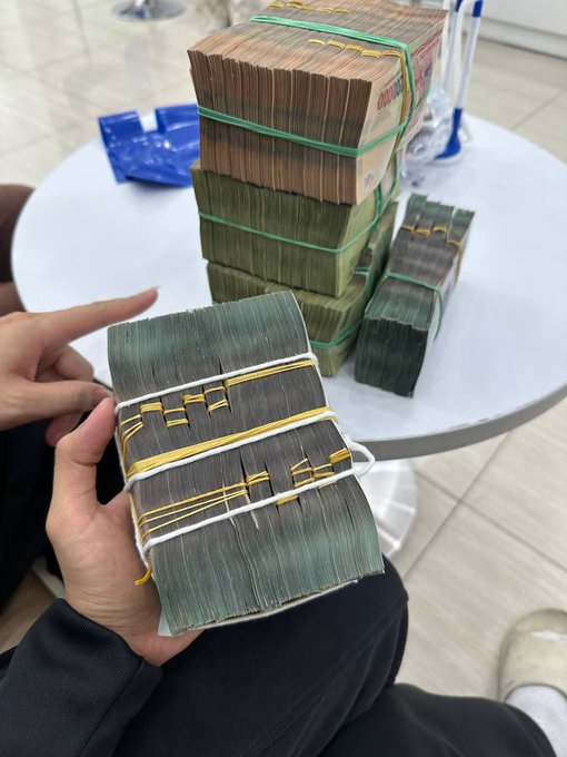 A person holds a thick bundle of cash secured with rubber bands, with additional stacks of banknotes resting on a round white table behind them. The image plays on the post's joke about "DCA-ing BTC" (Dollar Cost Averaging into Bitcoin), humorously suggesting that trading crypto could leave you with bundles of cash like these—or perhaps the opposite, given the playful "good vibes" tone of the message.