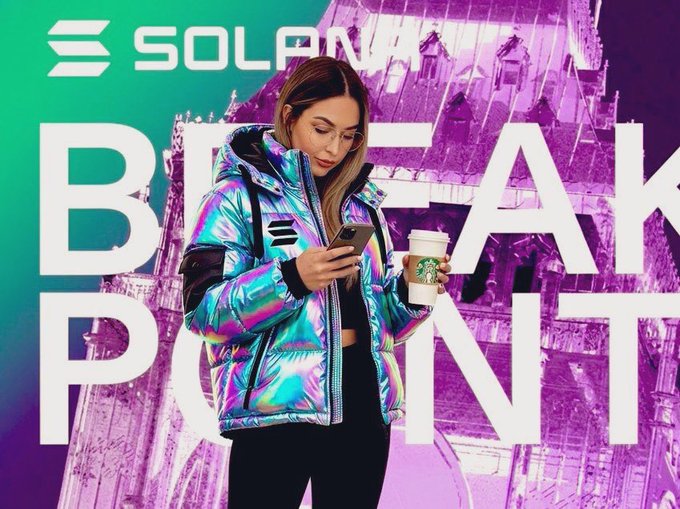 The image features a woman standing next to a building with a purple background. She is wearing a coat, holding a cup of coffee, and looking at her cell phone. The text "BREAKPOINT" can be seen in the image as well.