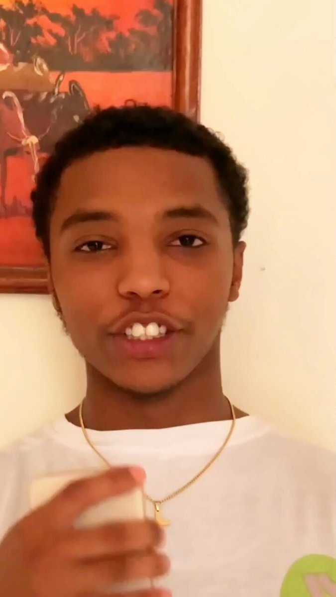 The image features a young man wearing a white t-shirt, holding a cell phone up to his face as if taking a selfie or recording a video. The background of the photo shows a picture frame with an orange border, which adds some color to the scene. The caption provided in the image is related to the post about OneFootball Club and how it connects football fans through digital identity and community participation on social media platforms like Twitter and Instagram.