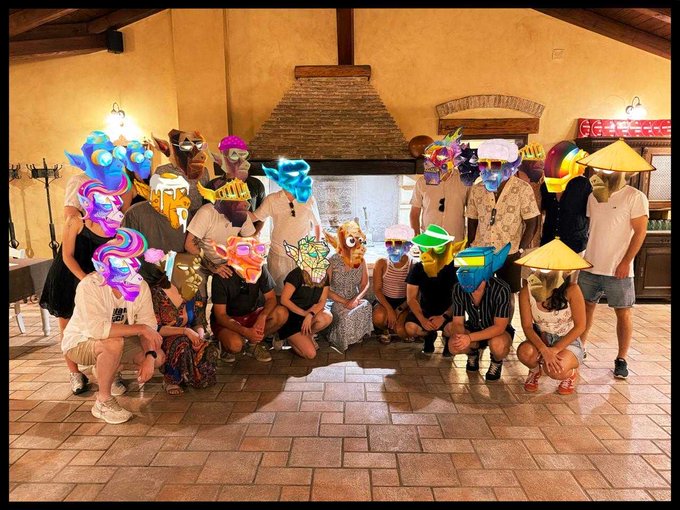 The image shows a group of people posing for a photo, all wearing masks that are colorful and unique. The masks cover their faces completely, making them look like characters from a video game or an online party. They are gathered around a fireplace, which adds warmth and coziness to the scene. The post about Solana seems to be related to this gathering of friends who have come together for a fun and memorable experience.